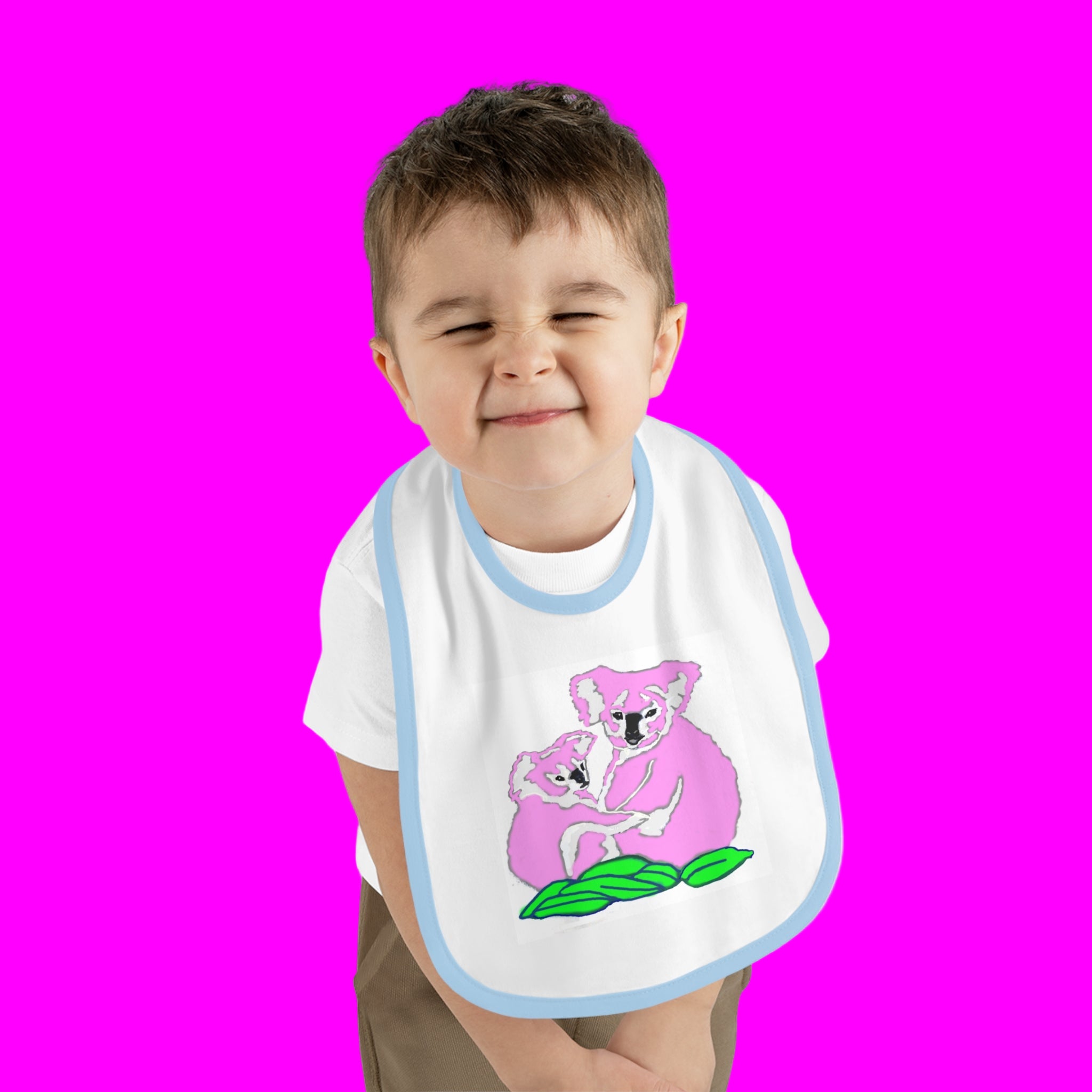 Child wearing a bib with a pink koala design on a pink background