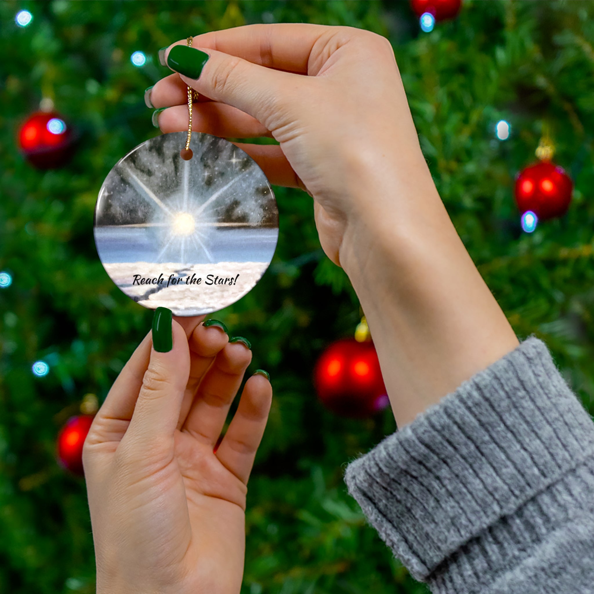 Hand holding a reflective ornament with 'Reach for the Stars!' text against a Christmas tree background.
