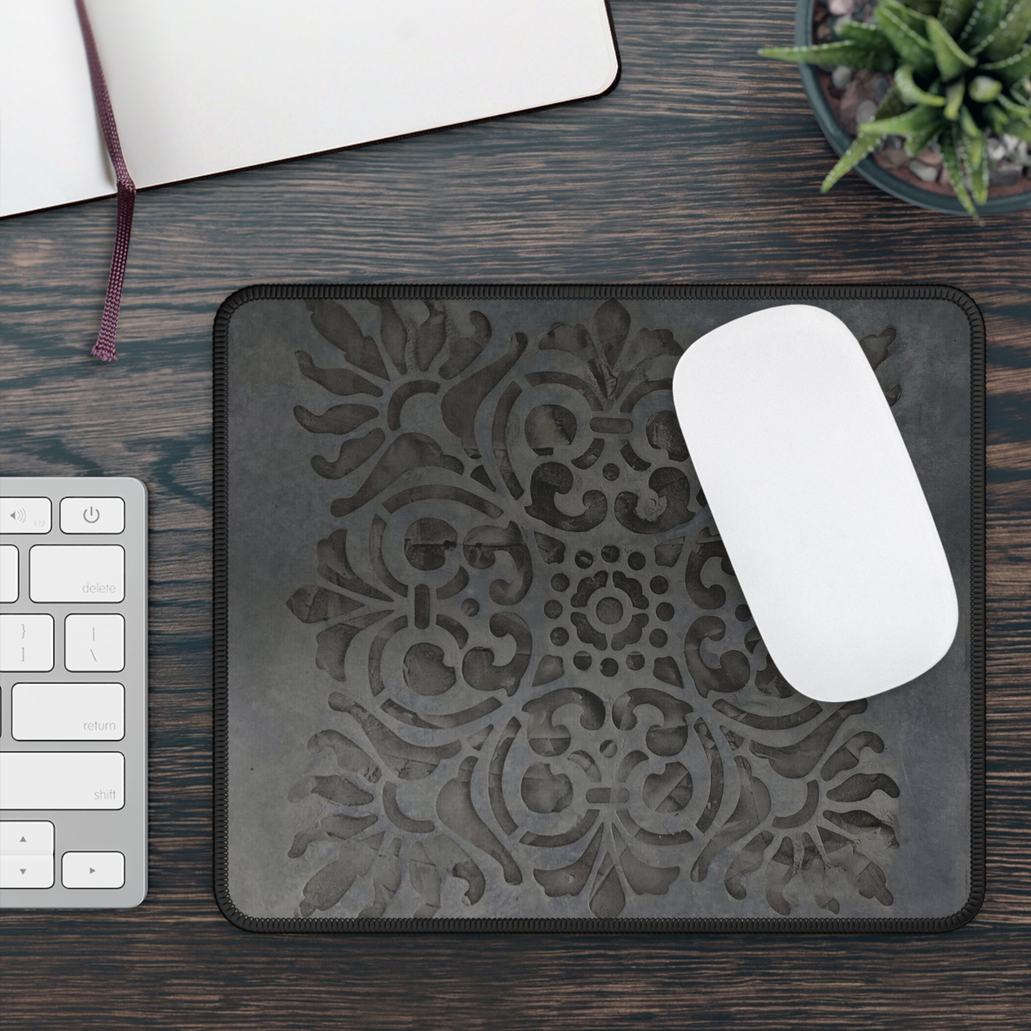 Decorative mouse pad with a white mouse on a wooden desk with a keyboard and plant.