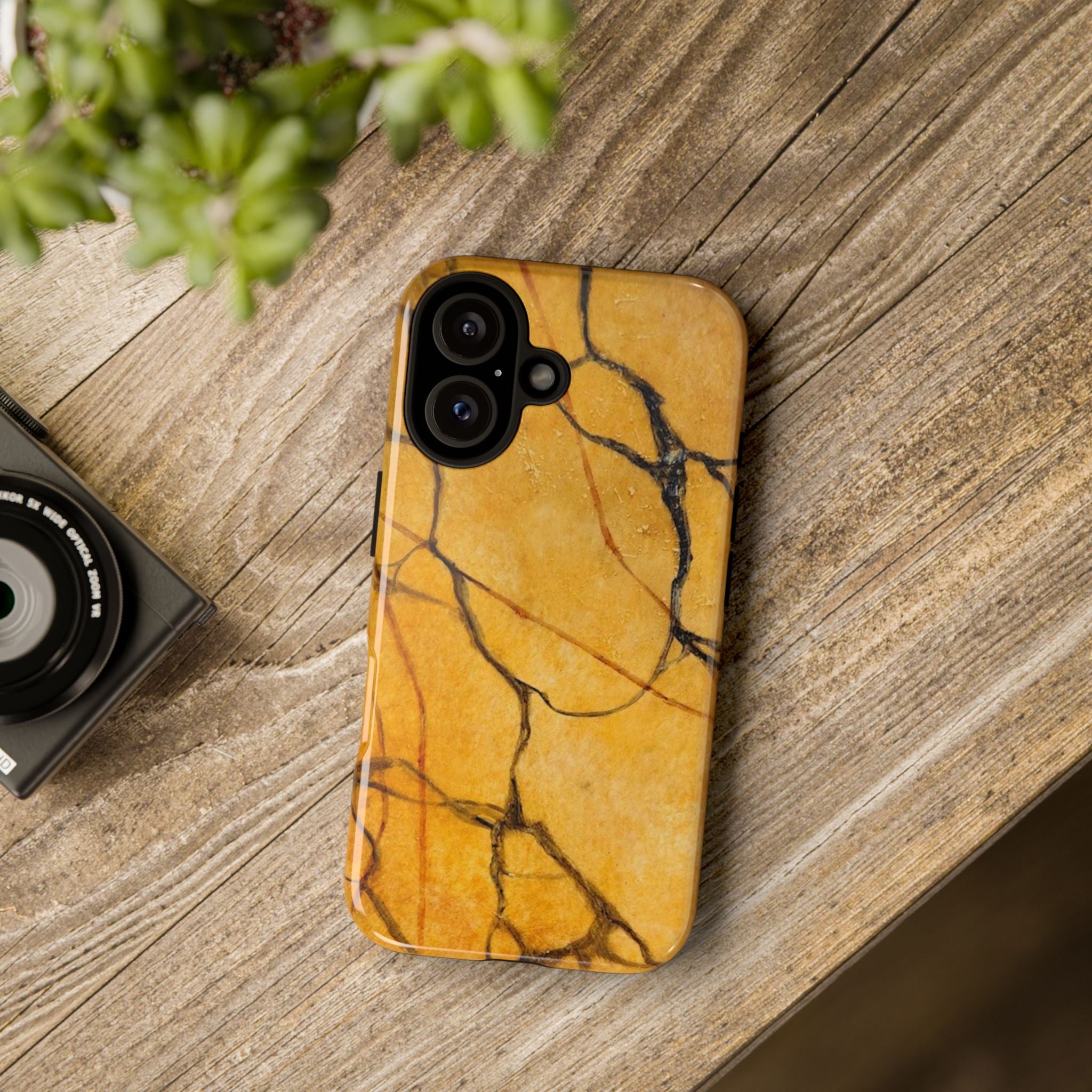 Phone case with marble pattern on a wooden surface next to a camera and plant