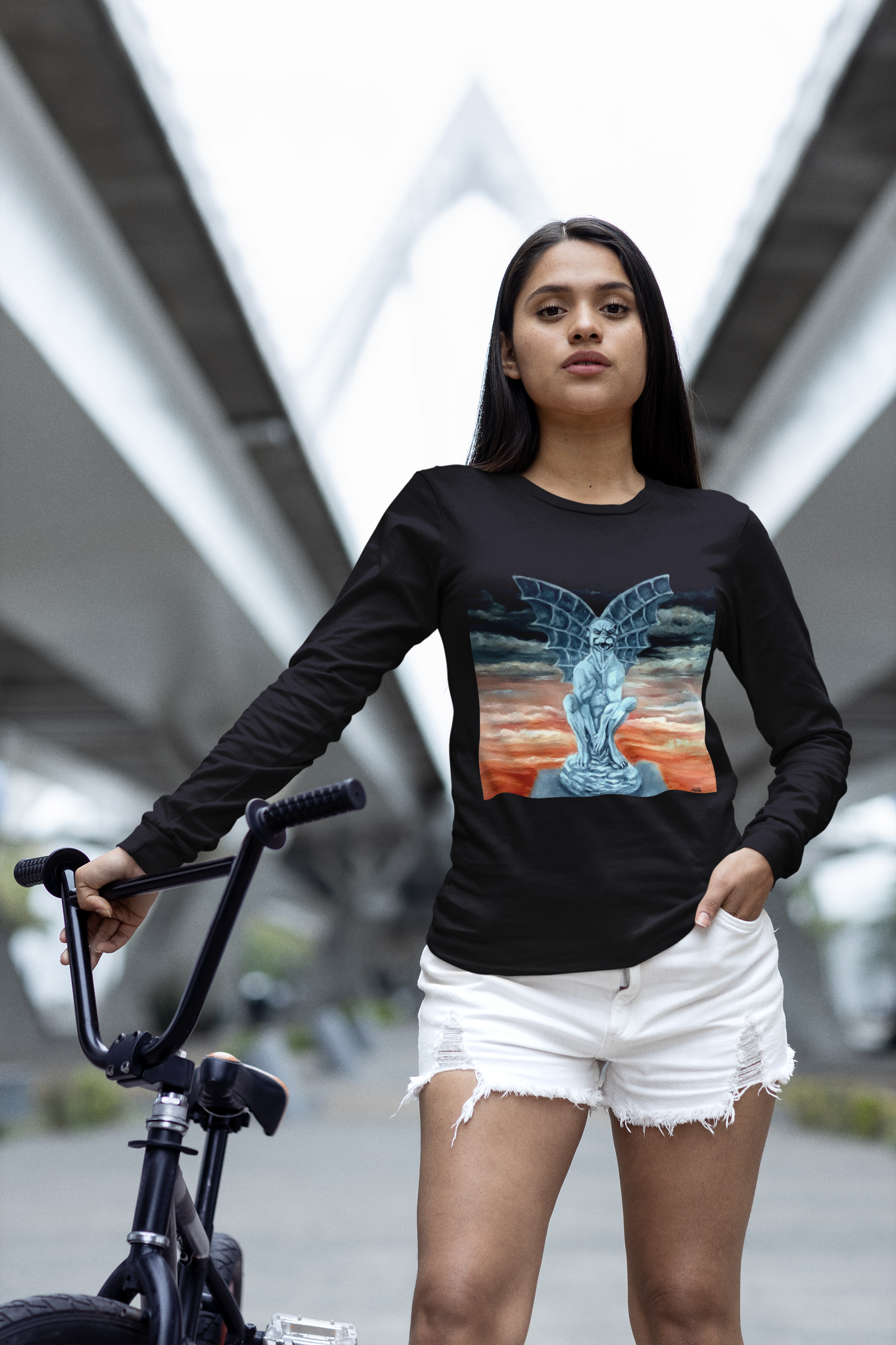 Girl  wearing a black long-sleeve shirt with a colorful Gargoyle design, standing next to a bicycle in an urban setting.