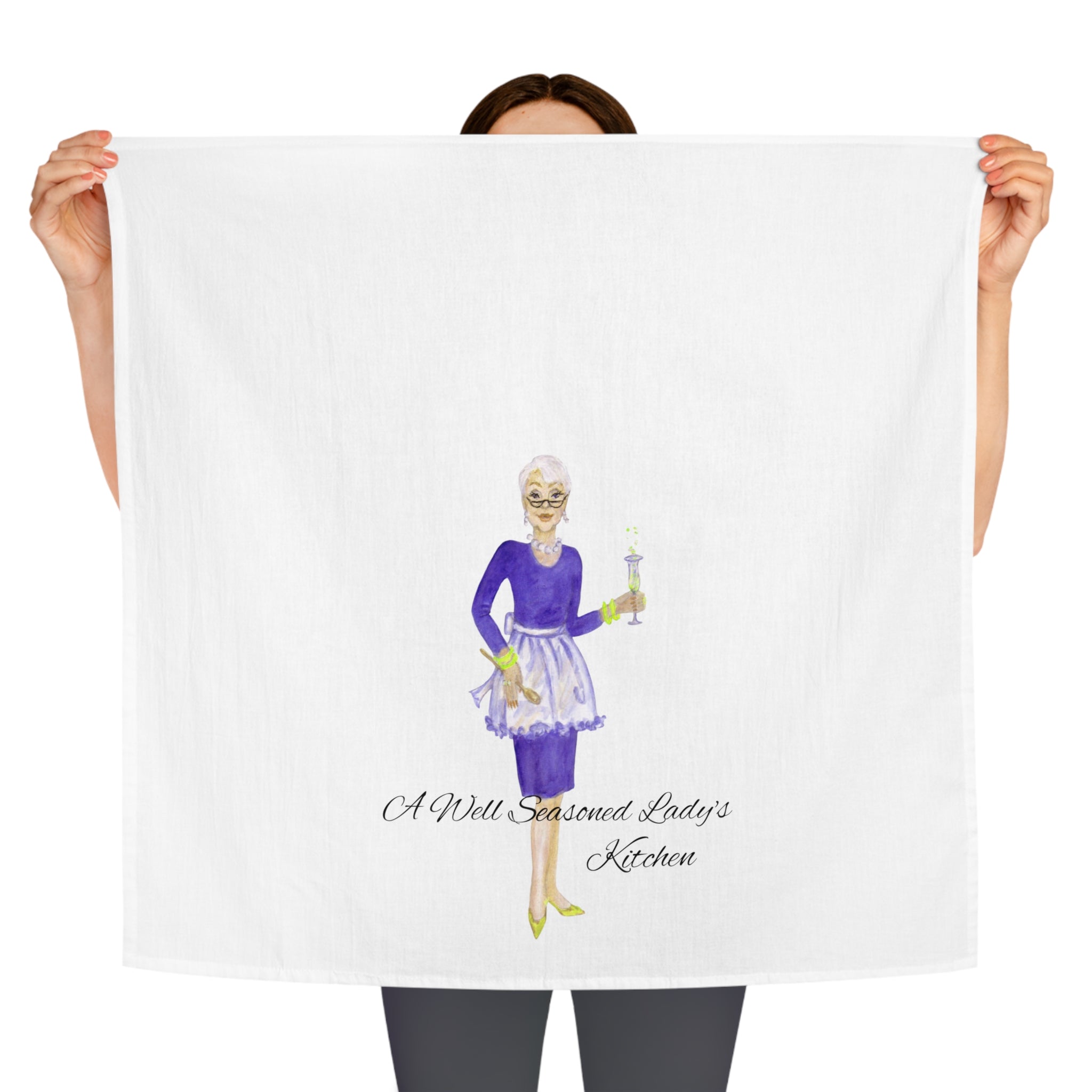 Person holding a towel with a graphic of a woman and text 'A Well Seasoned Lady's Kitchen' on a white background