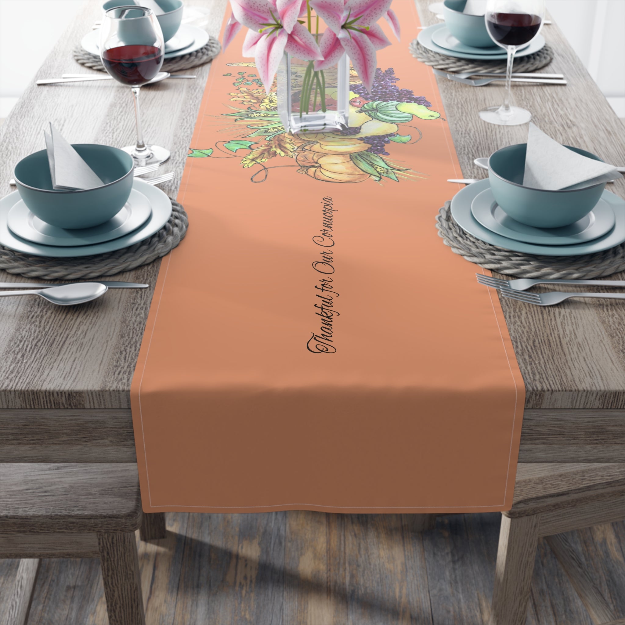 Table setting with a light orange table runner featuring cornucopia designs and text on a wooden table.