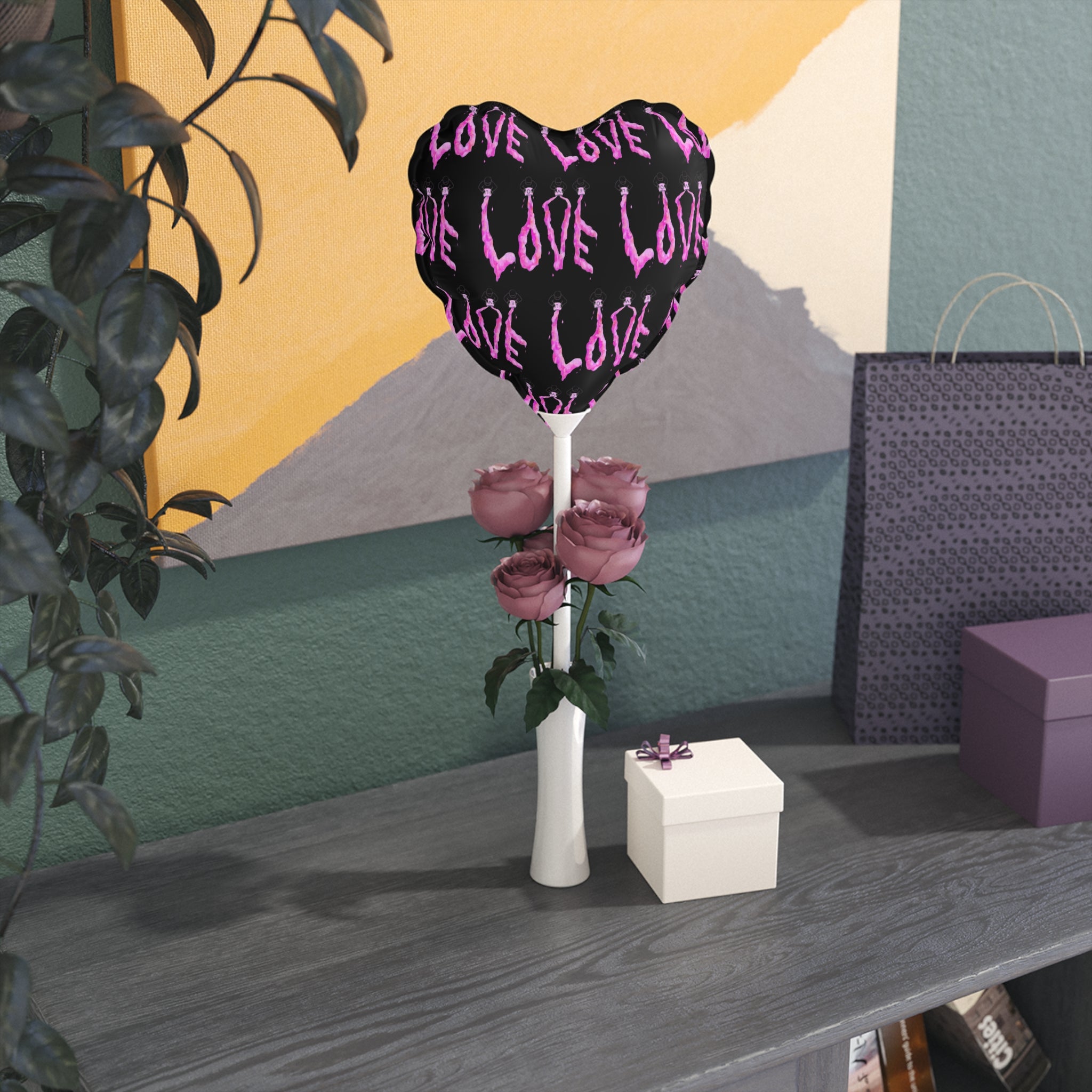 Heart-shaped balloon with 'LOVE' text, vase with flowers, and gift box on a table against a colorful wall.