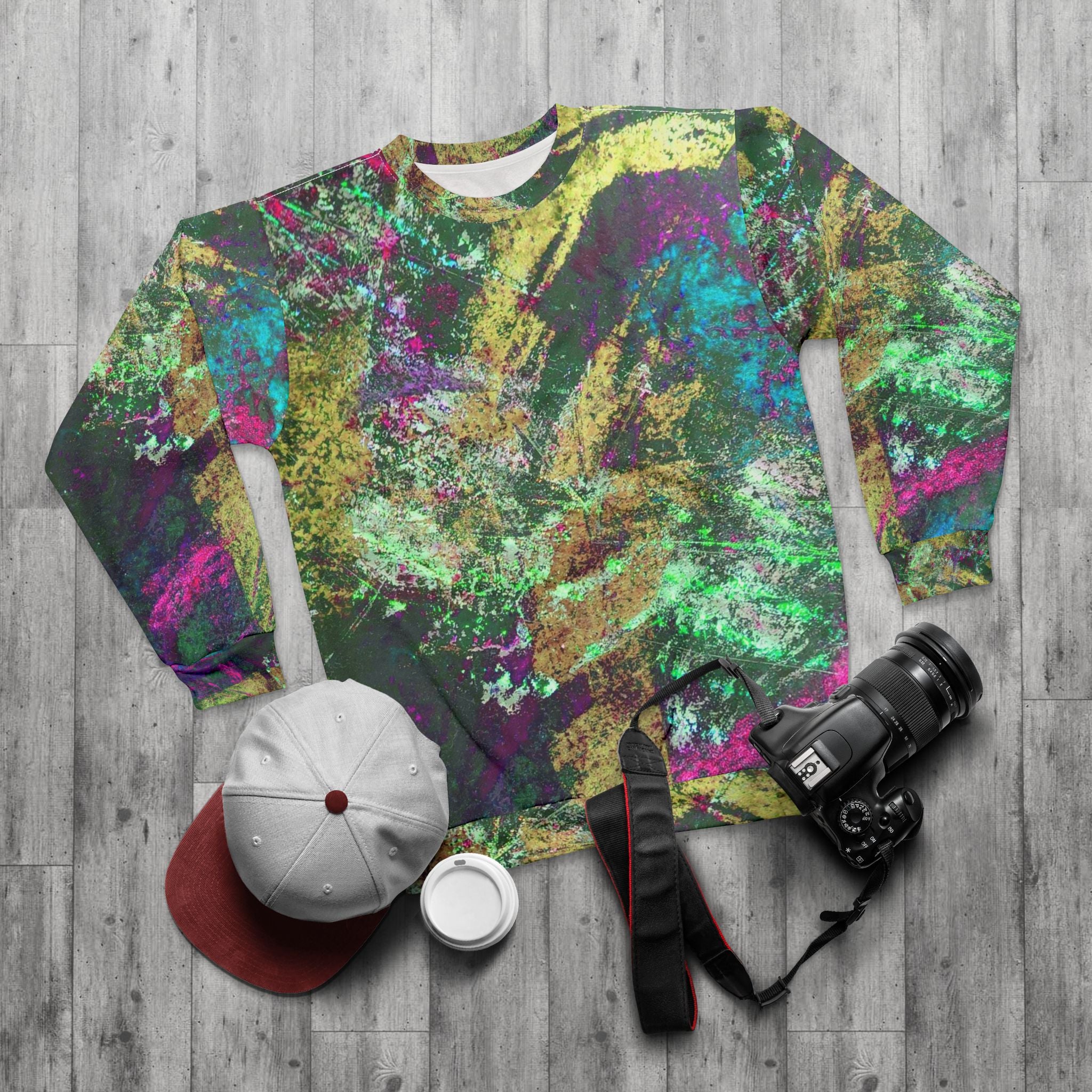 Colorful camouflage-patterned shirt on a wooden surface with a cap, camera, and bottle.