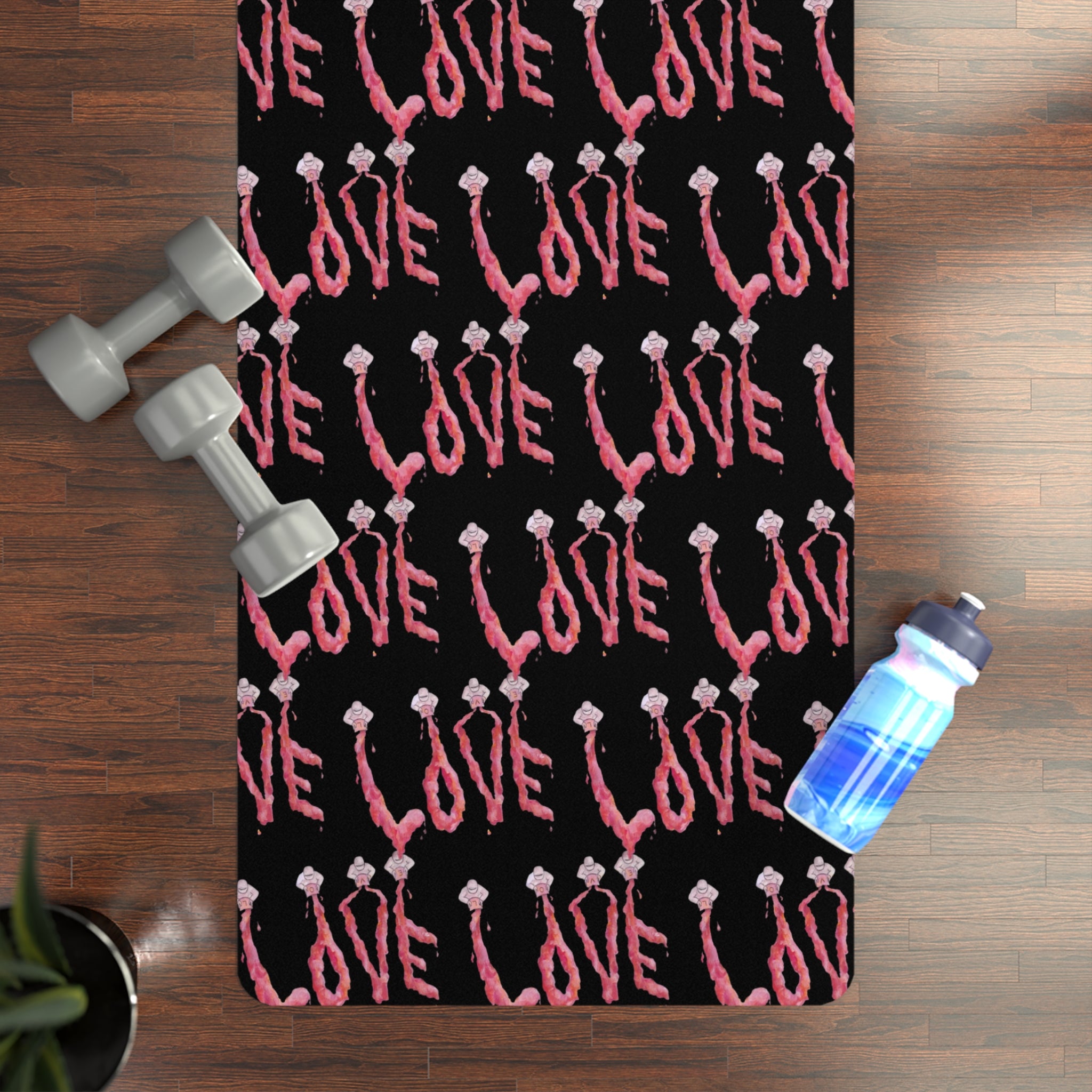 Black yoga mat with pink 'LOVE' text on a wooden surface with dumbbells and a water bottle.