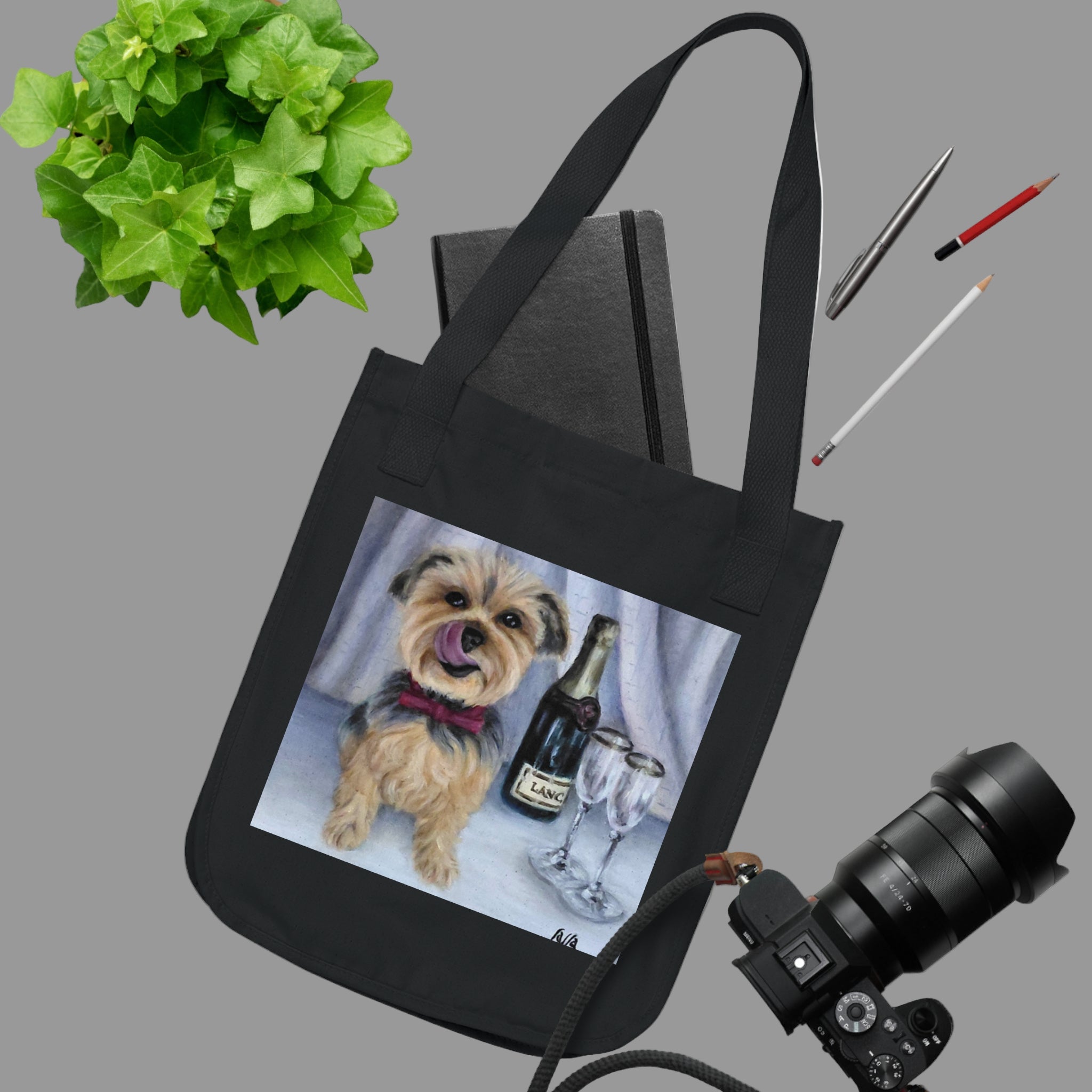 Black tote bag with a dog and champagne design, placed on a white surface with stationery items.