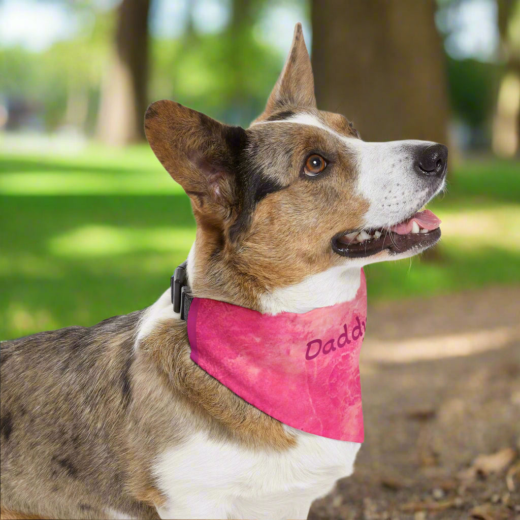 Dog wearing a pink bandana with 'Daddy' printed on it in a park