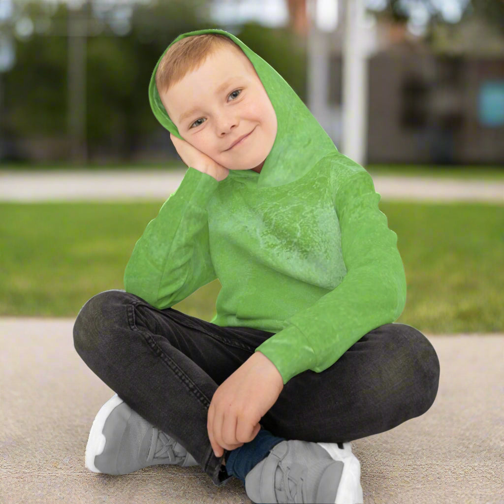 Child wearing a green hoodie sitting on sidewalk with outside background