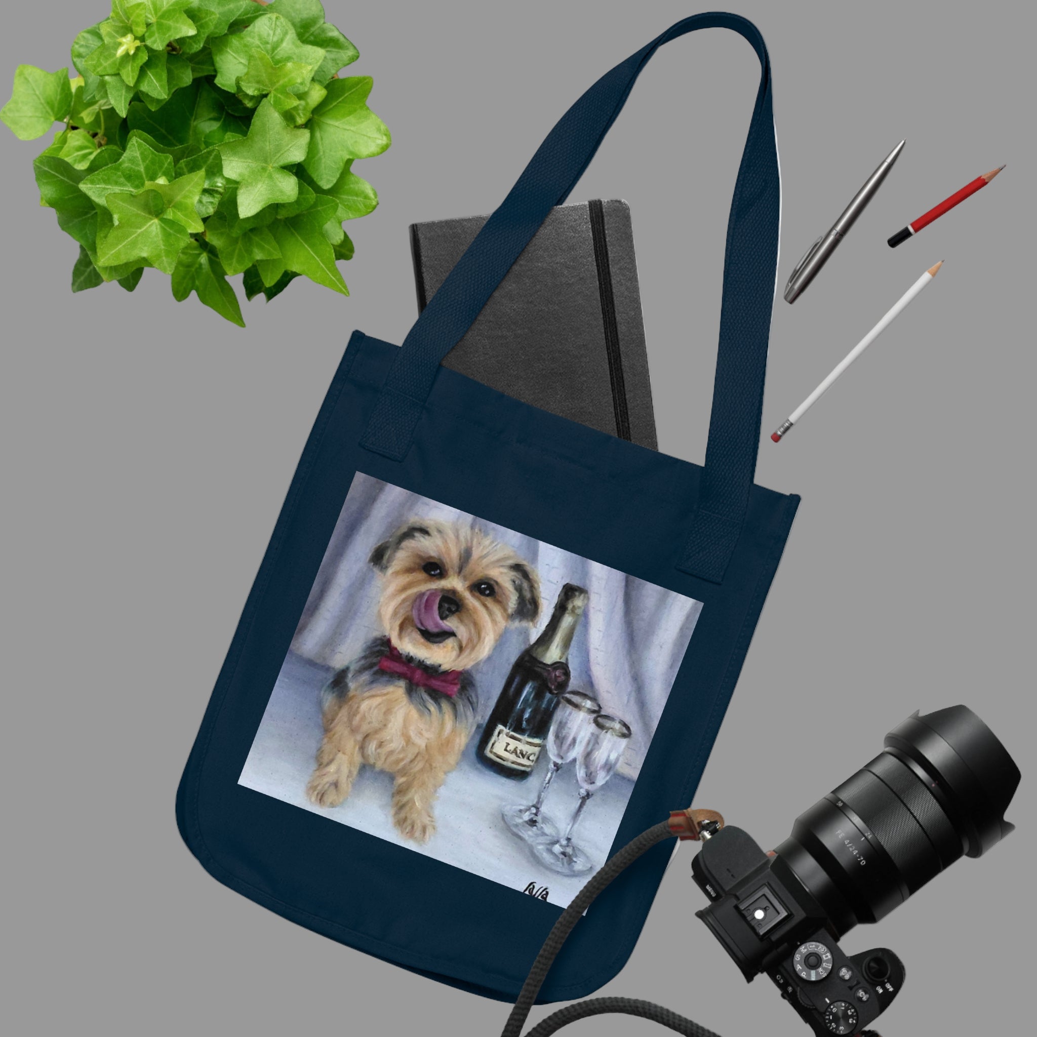 Navy blue tote bag with a dog and bottle design, placed on a white surface with stationery items.