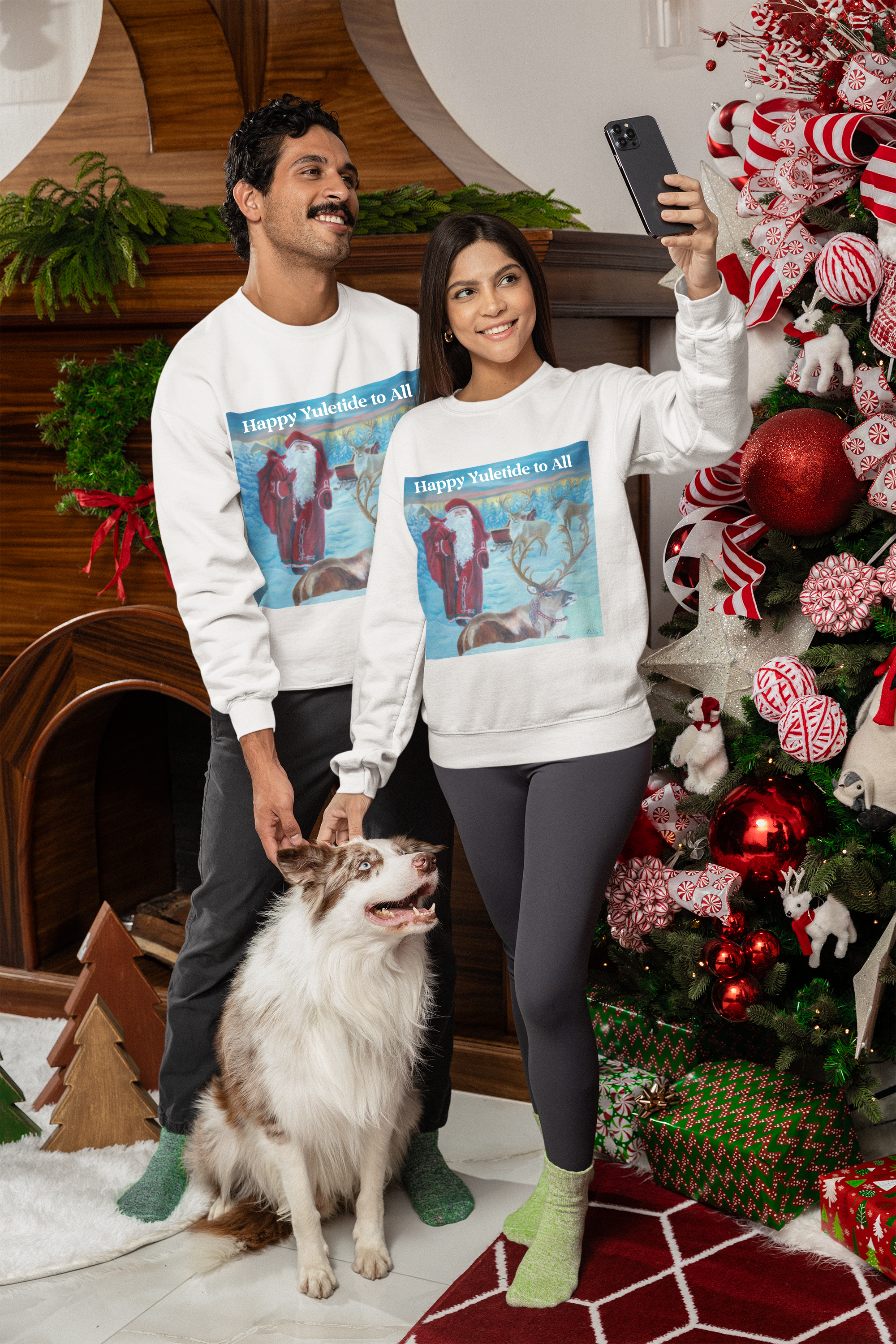 Two people and a dog wearing matching Christmas-themed sweatshirts in a festive setting with a decorated tree.