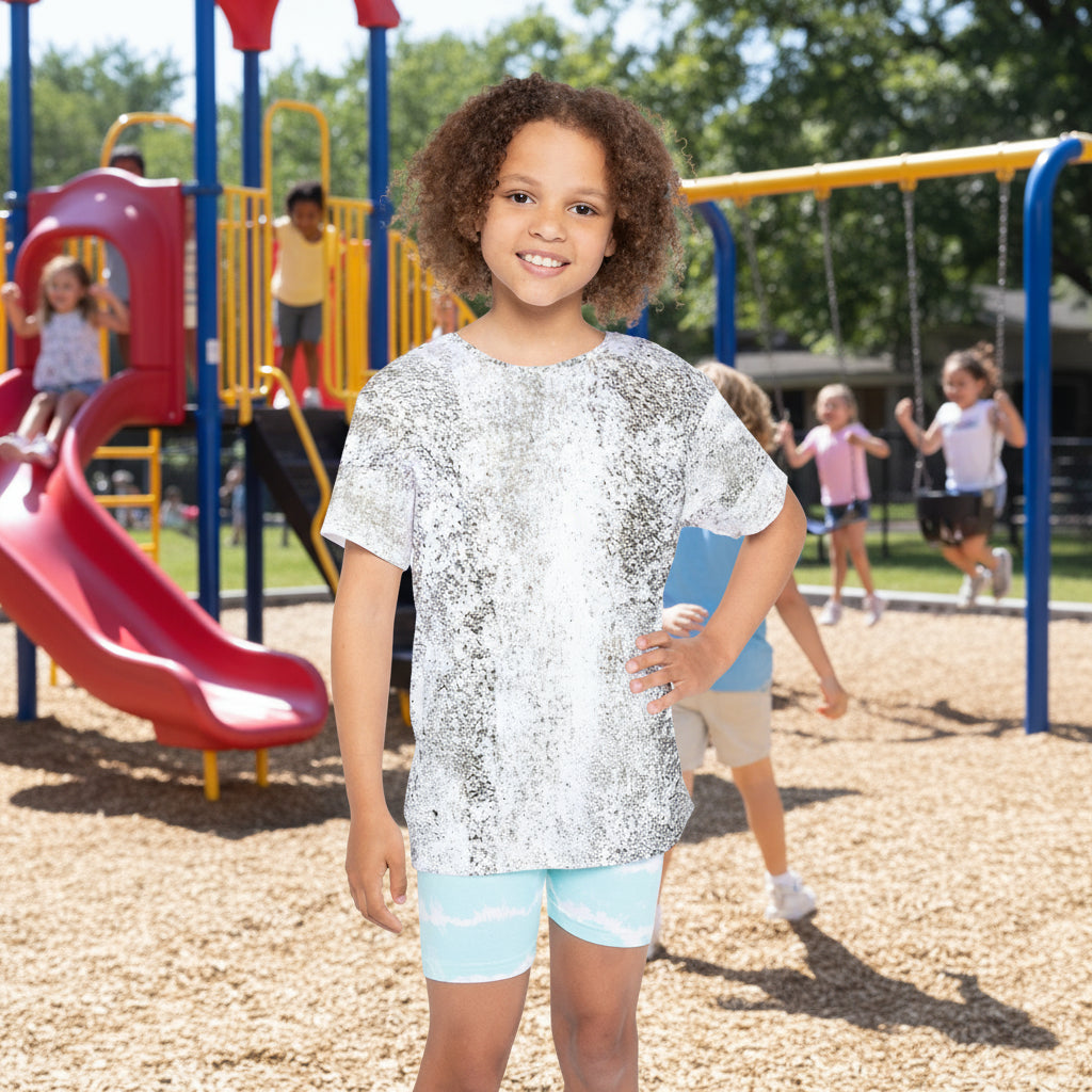 Child wearing a gray/white abstract print top and light blue shorts