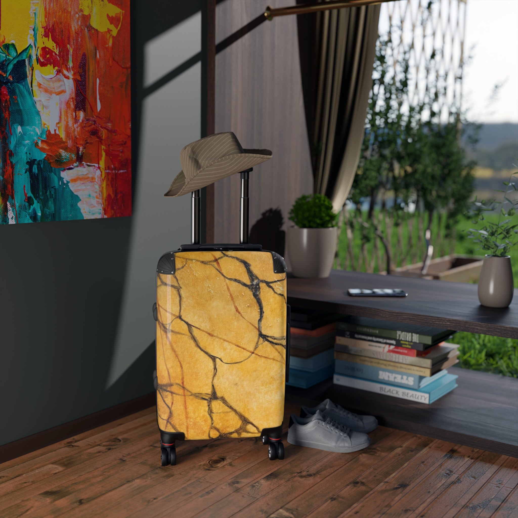 Gold marble-patterned suitcase with a hat on top, placed indoors near a window with a view of greenery.