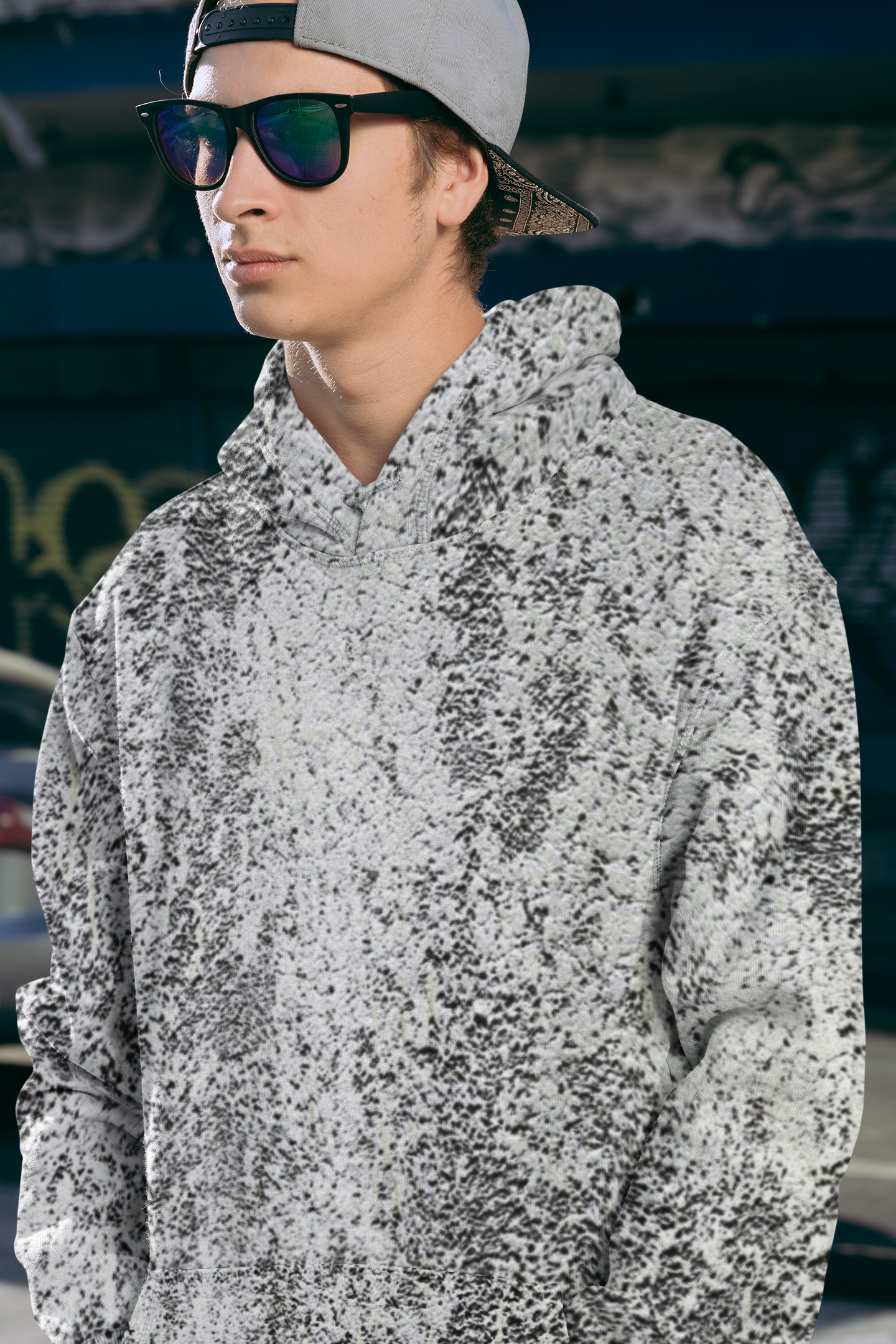 Person wearing a gray and white speckled hoodie with sunglasses and a cap.