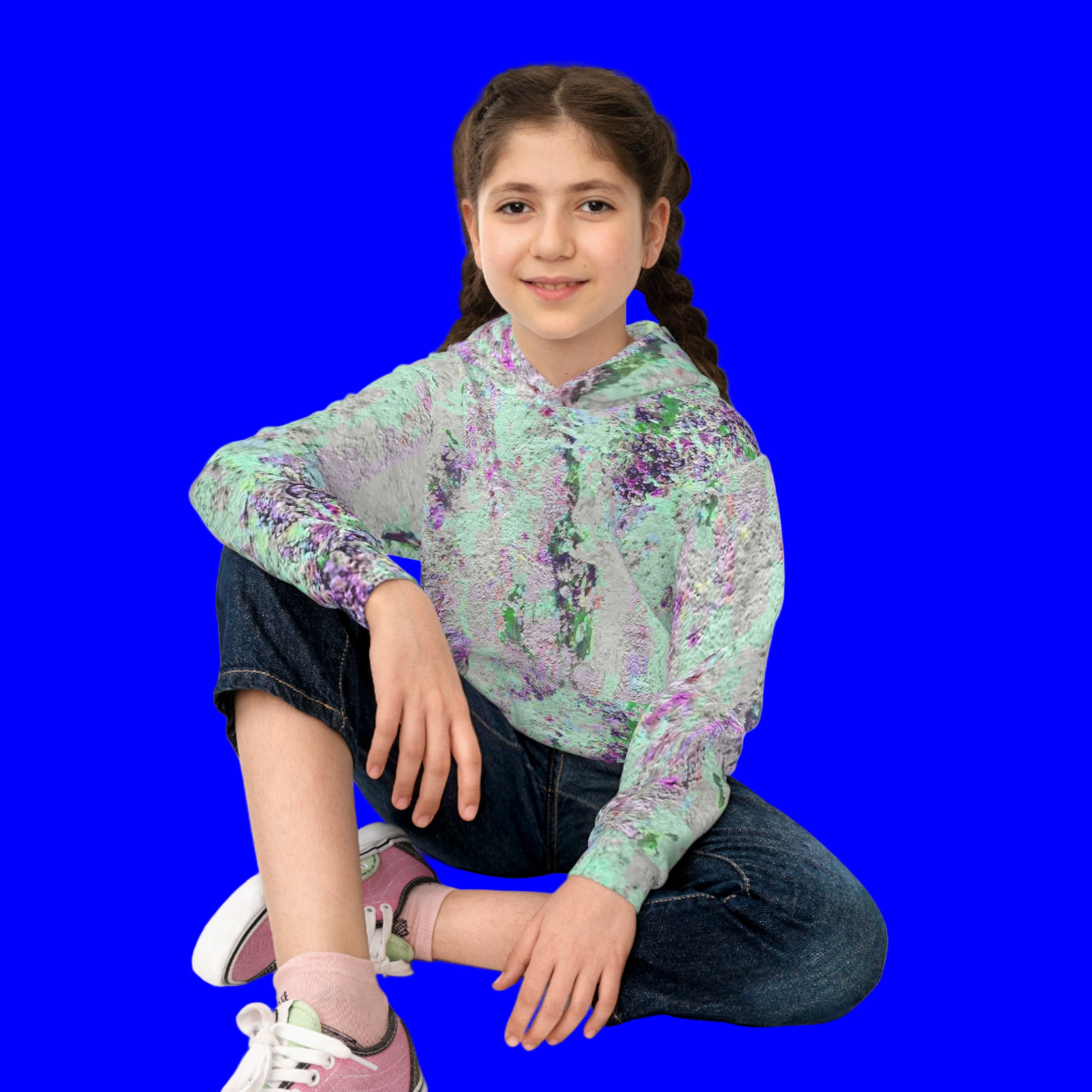 Young girl wearing an abstract art  hoodie sitting on the floor with a white background
