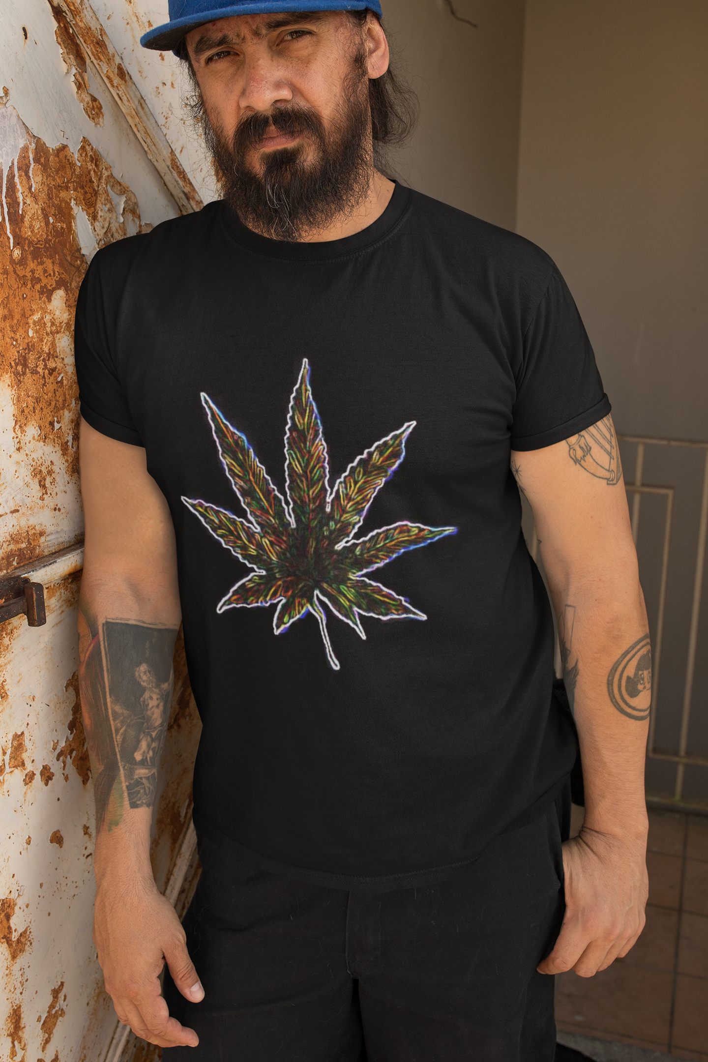 Man wearing a black t-shirt with a colorful cannabis leaf design, leaning against a wall.