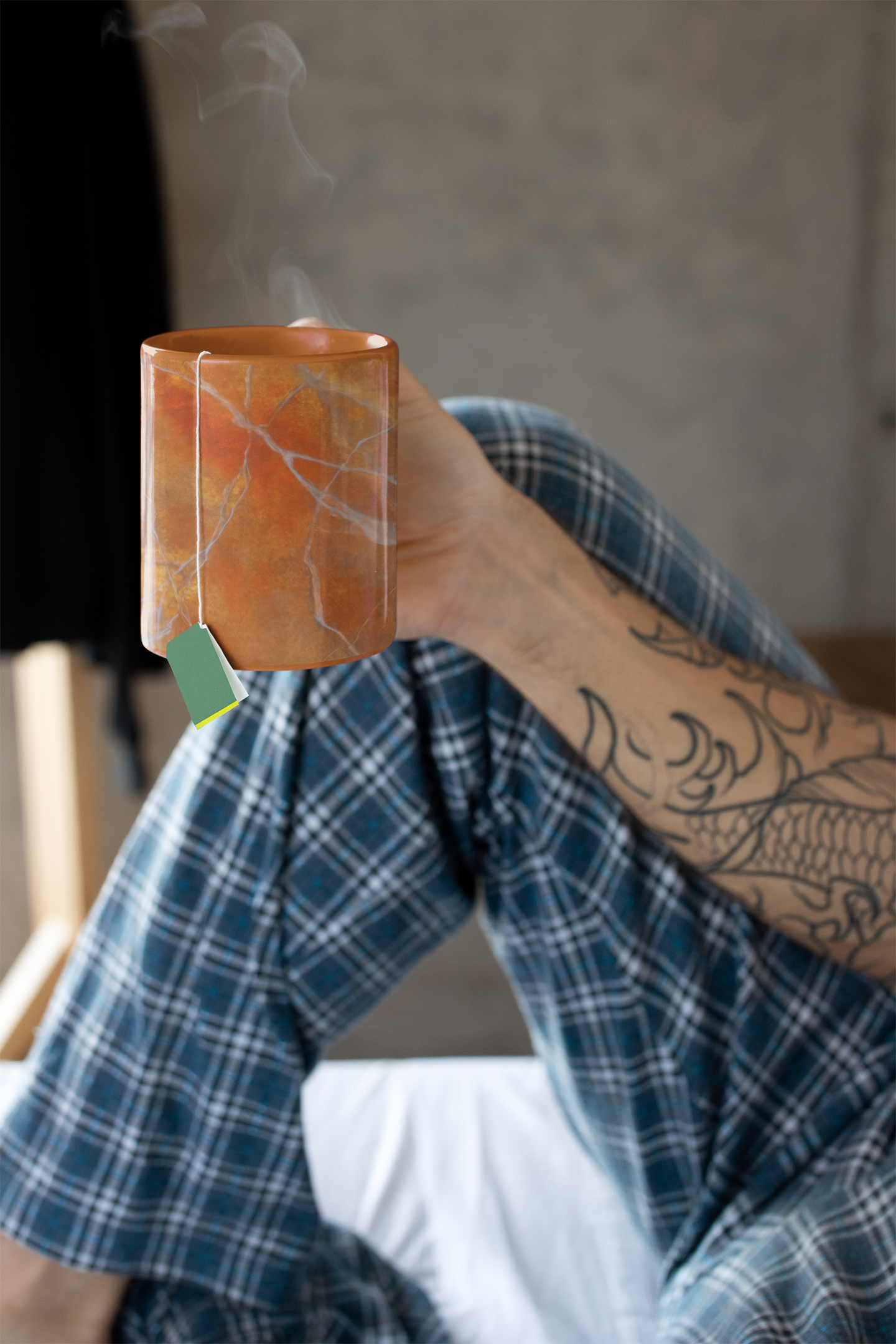 Mug in Red Orange Marble Design being held by a person relaxing in bed with tea.