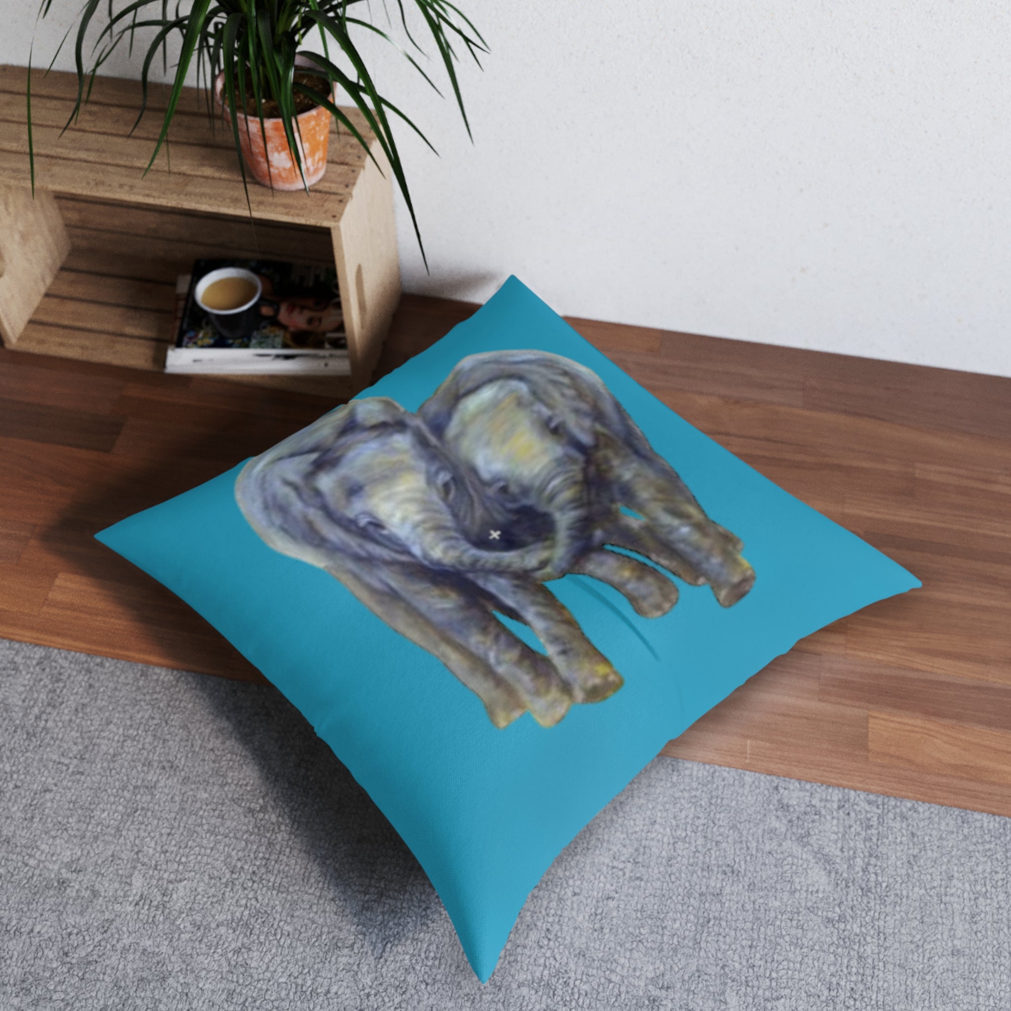 Decorative pillow with elephant design on a blue background, placed on a wooden floor.