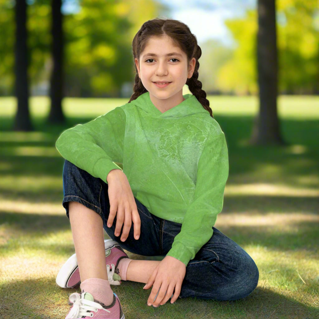 Young girl wearing a green hoodie and jeans sitting on the ground in a park