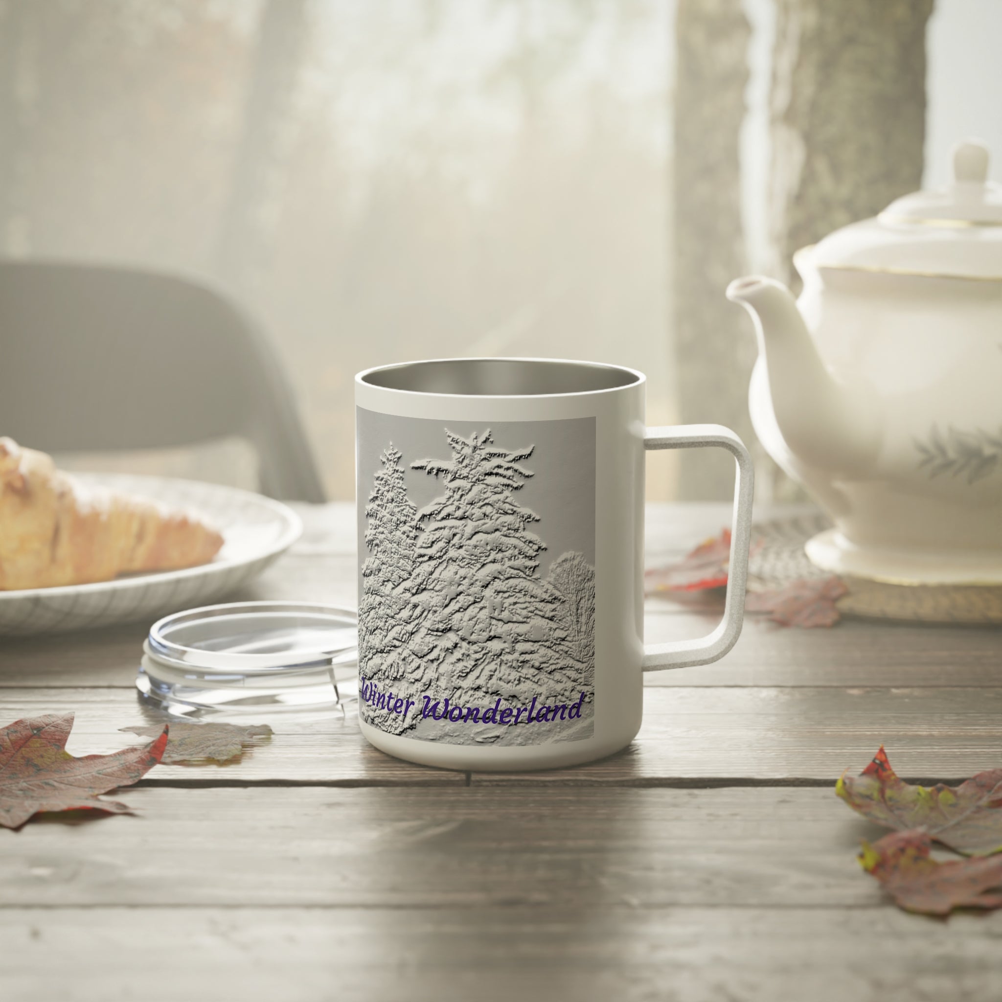White mug with tree design and 'Winter Wonderland' text on a wooden table with a teapot and croissant.
