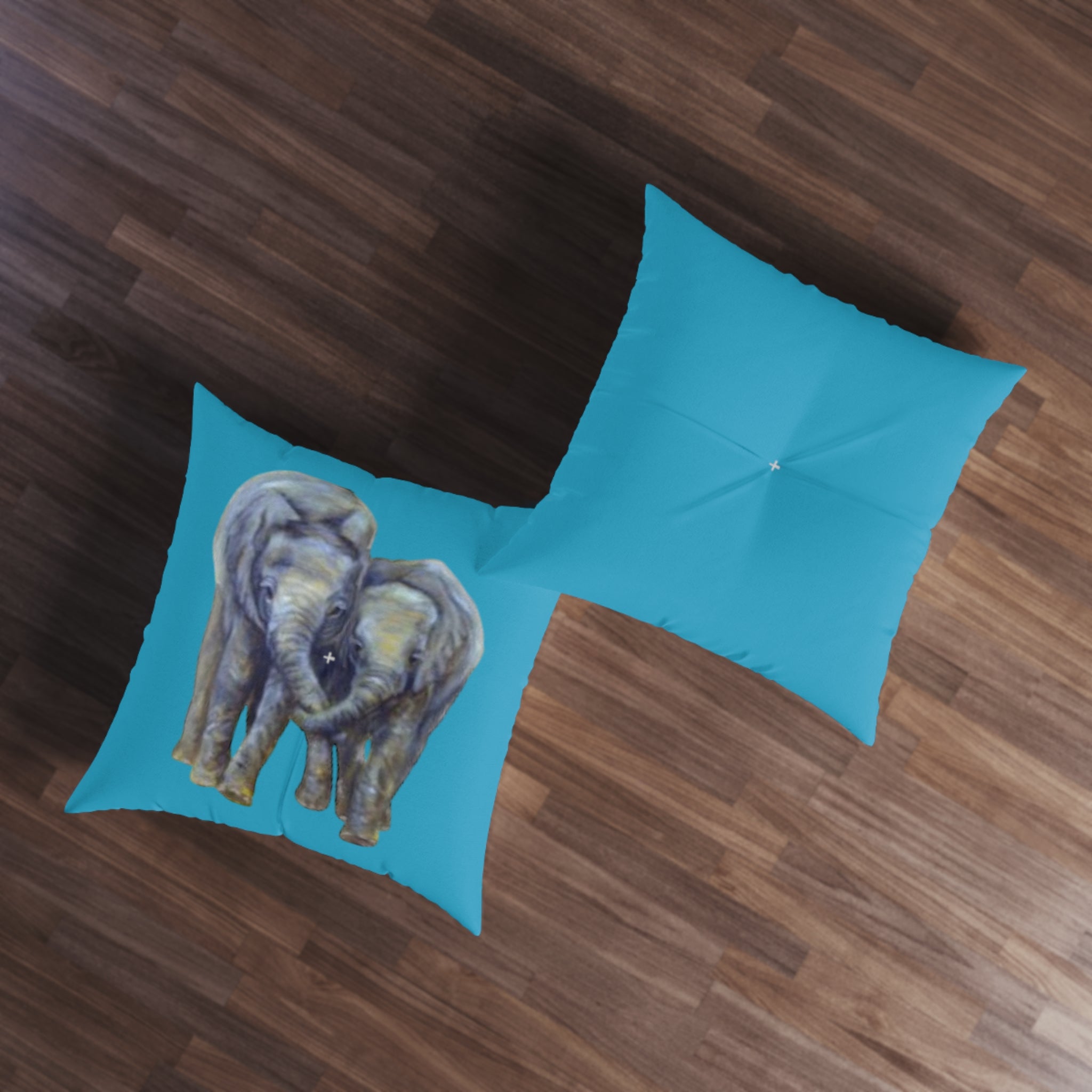 front and back of teal pillows with an elephant design on a wooden floor
